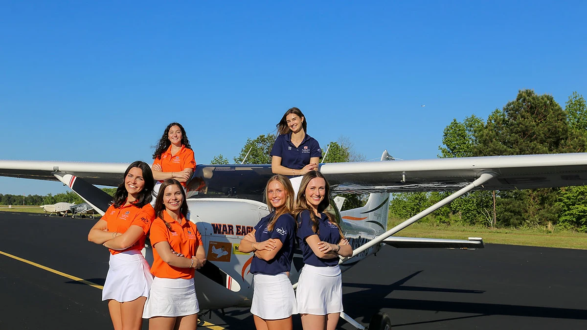 A group of five people are smiling beside and on a small airplane on a sunny day.