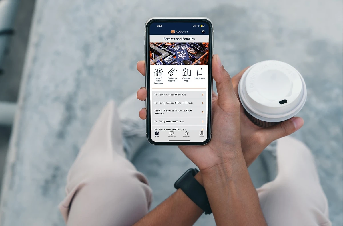 A person holding a smartphone with an app open for parents and families information, while also holding a coffee cup.