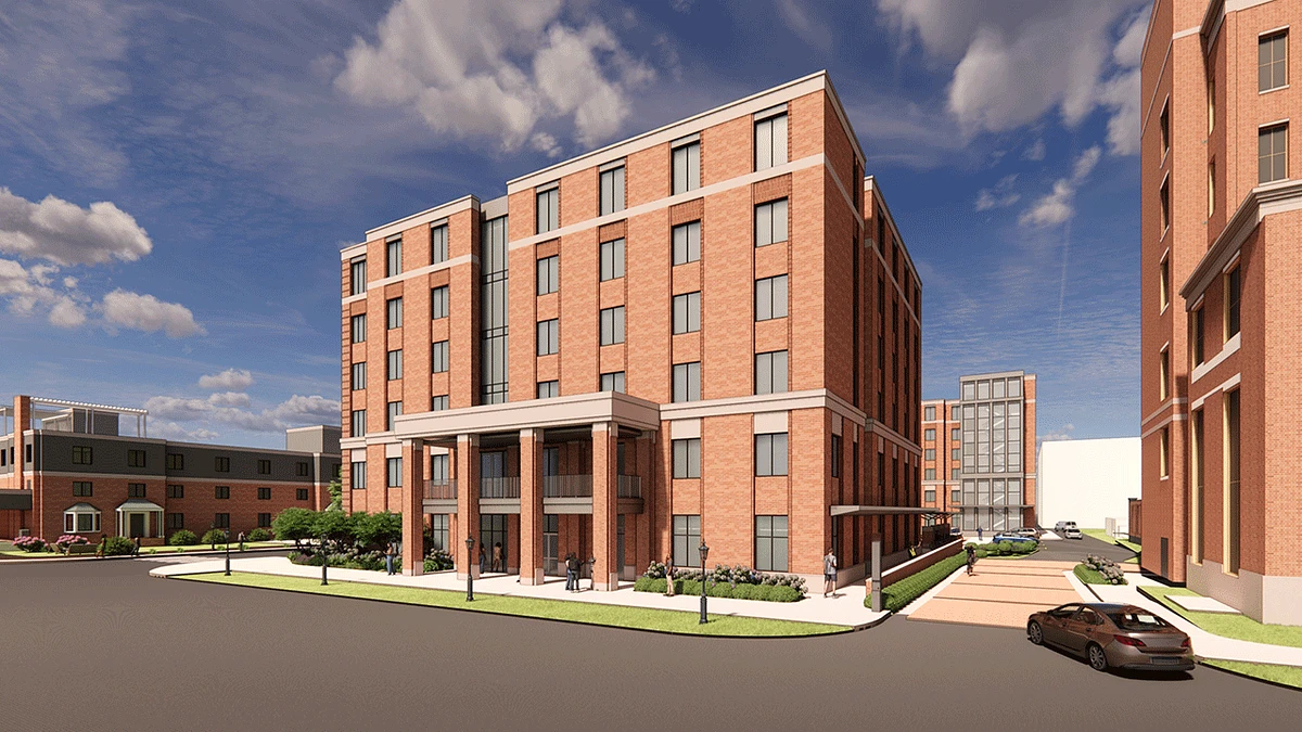 The image shows a modern multi-story brick building with large windows and an entrance porch, set against a backdrop of a clear sky with scattered clouds.